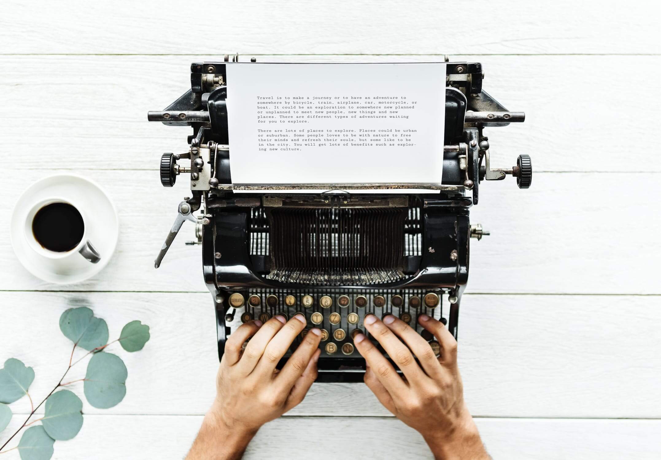 duas mãos digitando em uma máquina de escrever em cima de uma mesa de madeira com uma xícara de café do lado copywriting